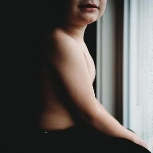 Close-up of a person's shoulder and part of their arm, looking out a window with natural light.