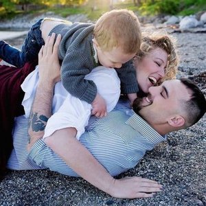 A family of three playing on a rocky beach, smiling and enjoying each other's company.