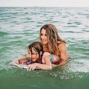 A woman and a young girl swimming in the ocean, with the woman holding the girl as they enjoy the water.