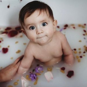 Baby in a bathtub surrounded by flower and petal-shaped bath toys and decorations.