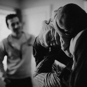 Three people in a black-and-white photo, two are hugging while one is smiling in the background.