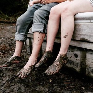 Two people sitting on a dock with their feet in the water, covered in mud.