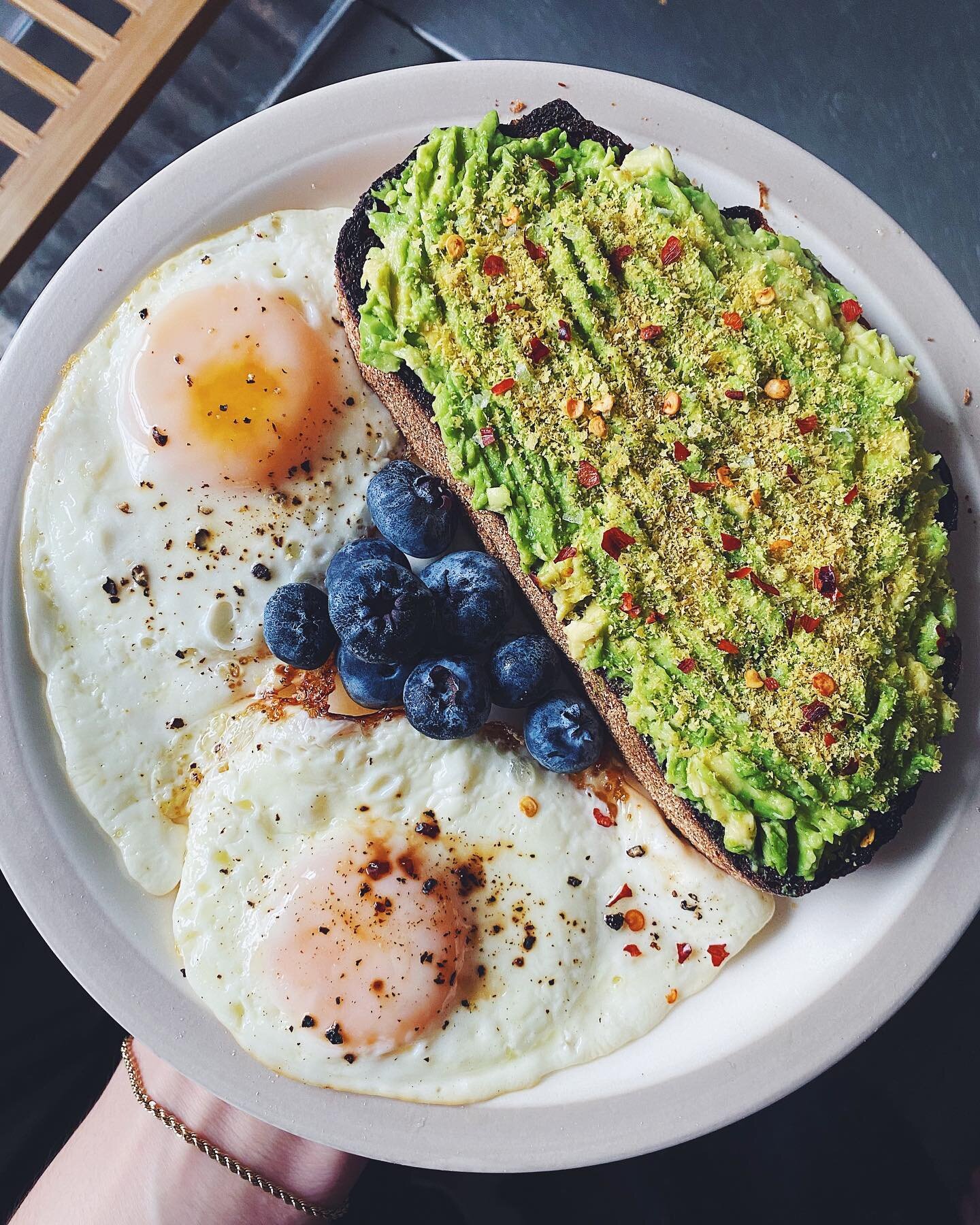 Avocado sourdough toast with nutritional yeast, red pepper flakes, flaky sea salt, and black pepper, two fried eggs and blueberries. 🥑🍞🫐🍳 Have you tried nutritional yeast? It&rsquo;s literally just yeast (often the same species used in bread- and