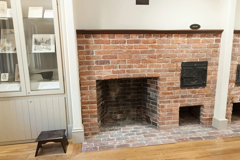 One of two original fireplaces, with custom built in cabinets flanking the hearth. Both cabinets are airtight to protect the artifacts on display. The finished building dimensions however did not match the drawings and specifications that were provided. Due to this variation being smaller than originally indicated it required the cabinet to be altered on site to fit. A new interior side panel was installed in the field, while maintaining the air seal and cutting the old exterior panel off, shrinking the entire cabinet by 2 inches. Cabinet construction across all of Lathrop Place consisted of Medex, which is a type of MDF designed to be water resistant and formaldehyde free to prevent off gassing which could degrade museum artifacts.