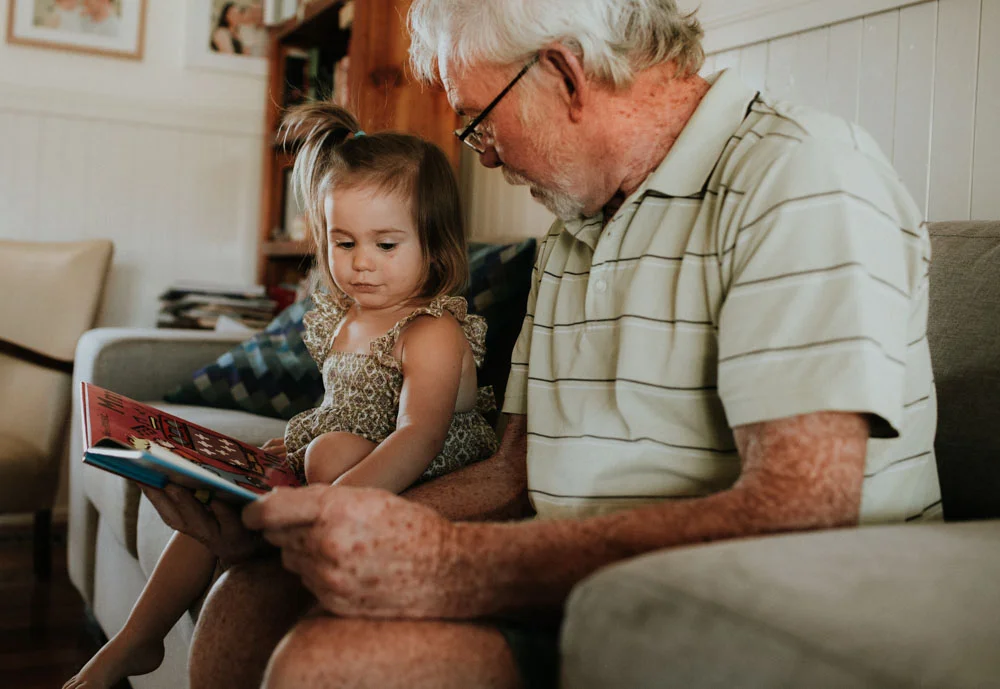 grandfather reading a book to grand daughter while visiting in their home in Gippsland
