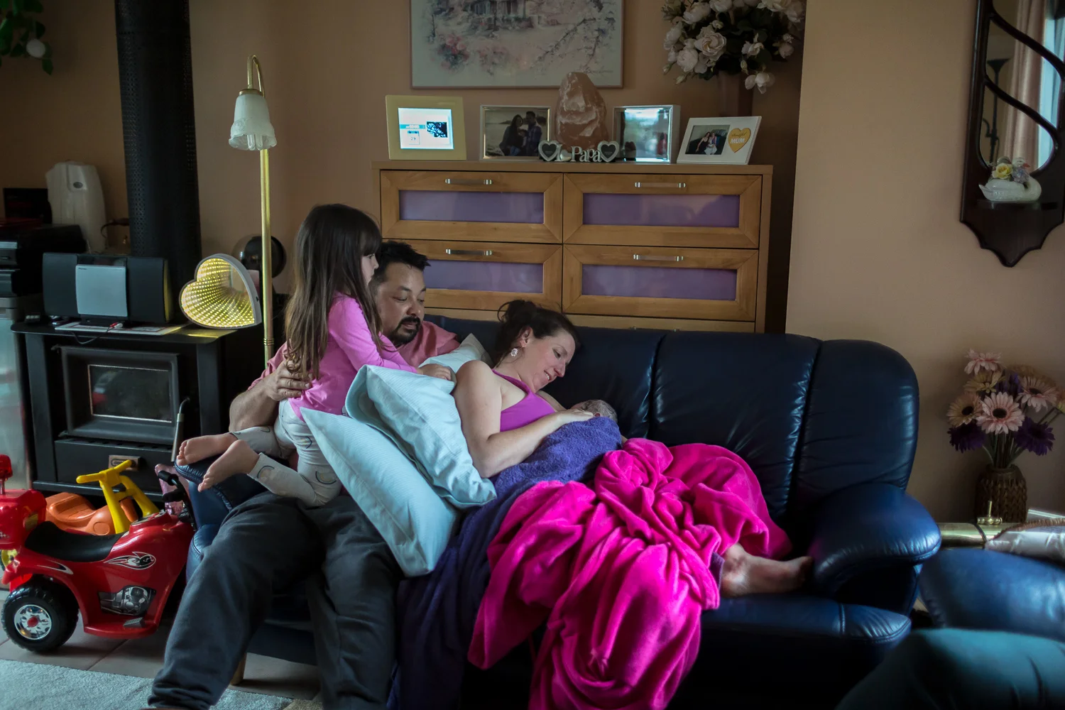 Whole picture birth. Family on couch soaking in the details of newborn baby in the golden hours after birth.