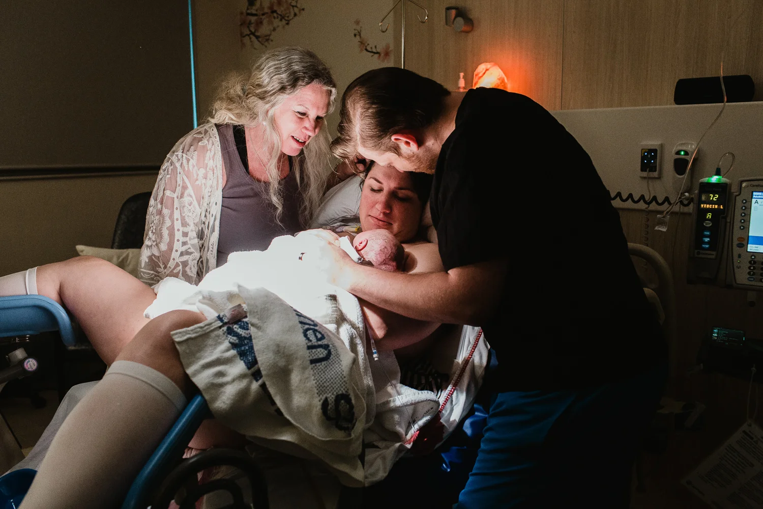 Family meeting newborn baby for the first time. Mother is in bed holding the newborn while grandmother and father and gazing down. Image from birth at Leongatha Hospital.