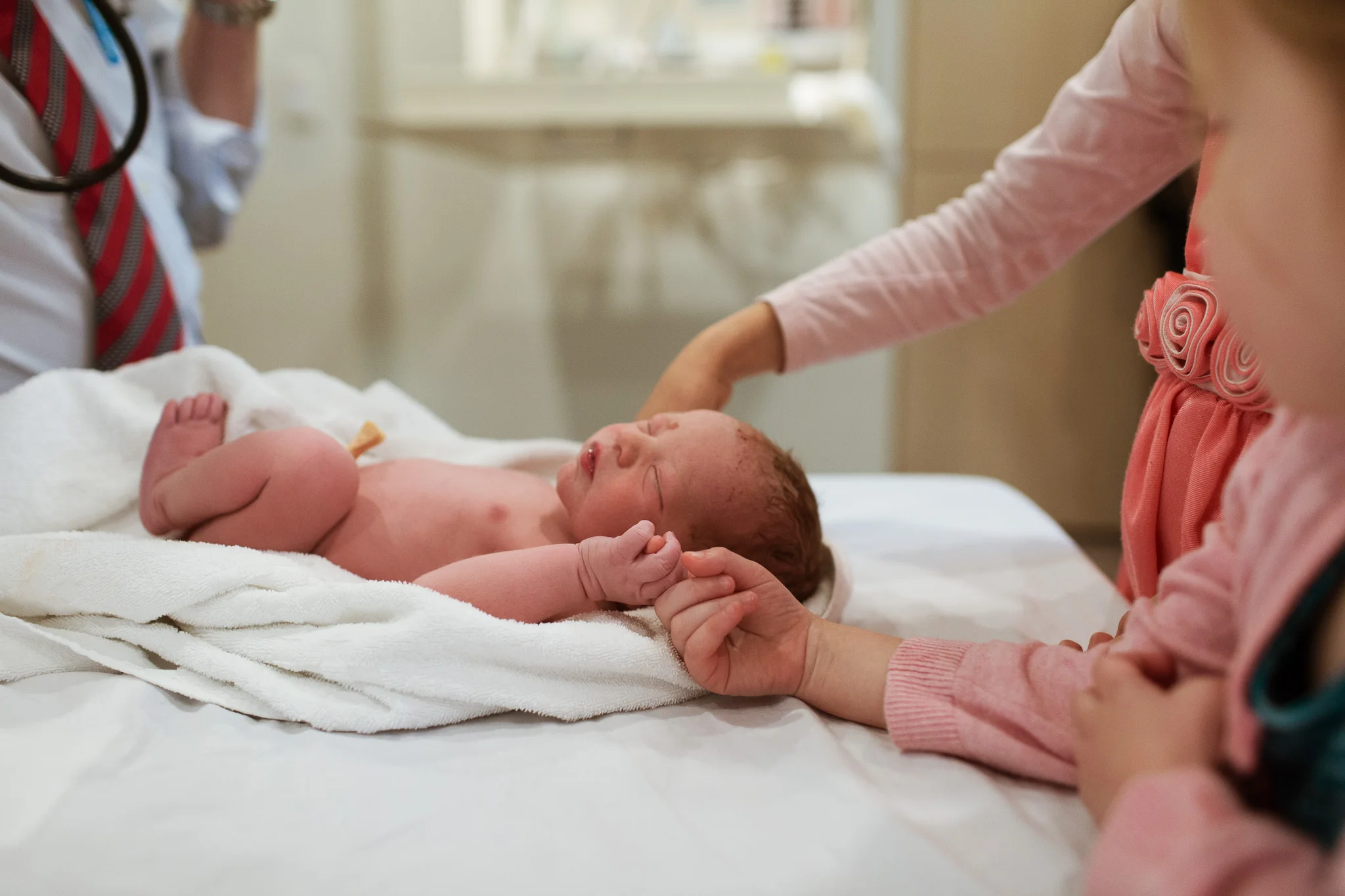 Siblings meeting their for the first time an hour after birth. Two big sisters are holding the hand of newborn who is laying on the bed at Mitcham Private Hospital.