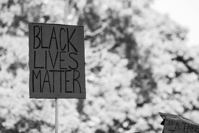 A black and white photo depicts signs at a Black Lives Matter protest. The primary sign reads “Black Lives Matter.”