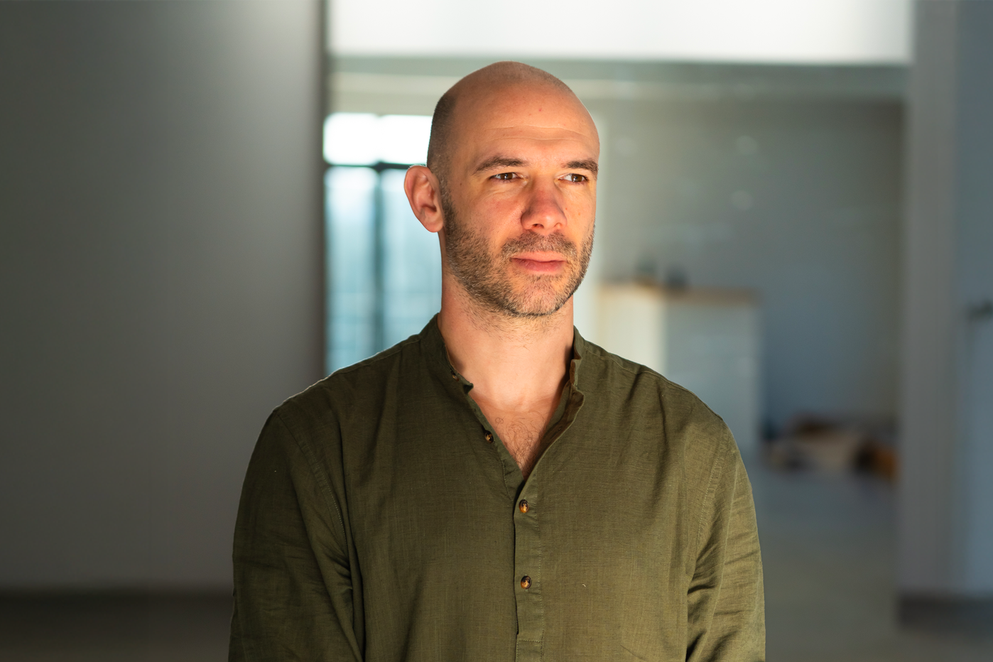 Homme avec une barbe, portant une chemise verte, regardant pensif dans une maison moderne
