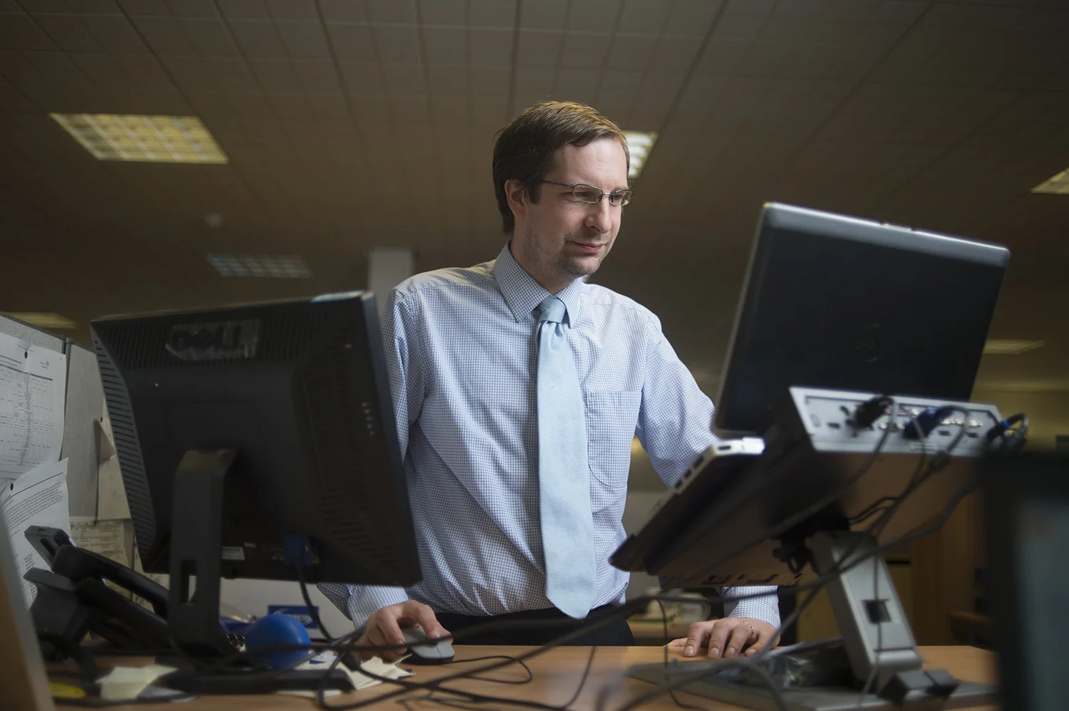 Viewed from behind the screens, a HSMA researcher looks at two computers at a standing desk.