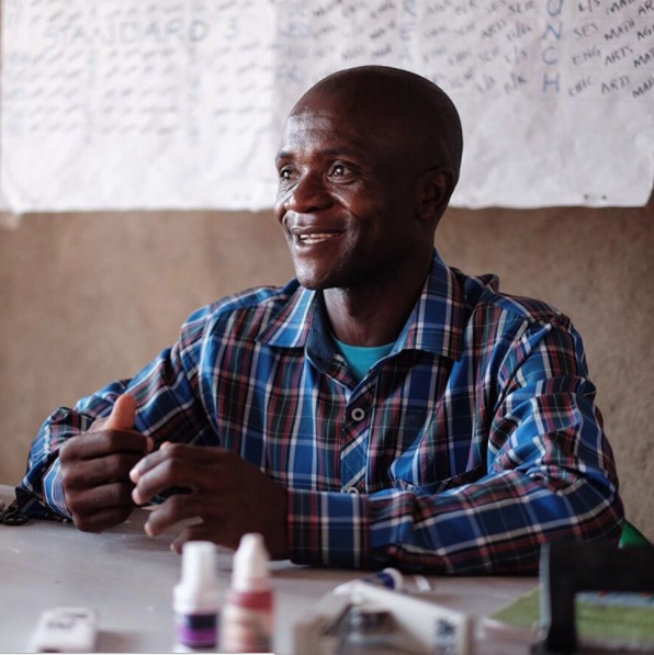 Our model taps into the energy and dedication of education leaders like this one, who grades compositions in the brightest corner of his classroom in a low-fee community school in Nairobi.