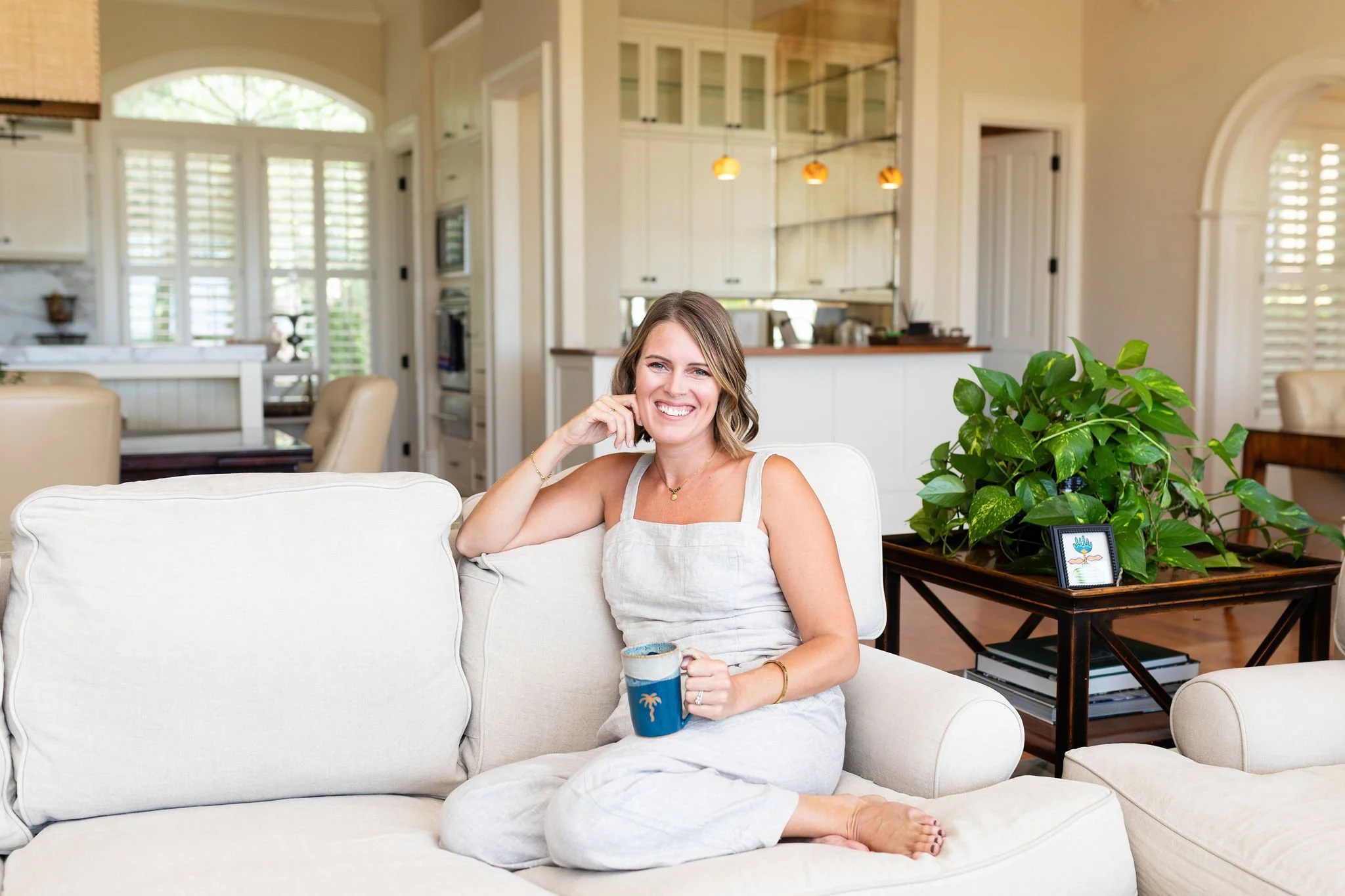 Callie Cullum, founder of The Look & The Feel, sitting on a white couch holding a handmade coffee mug