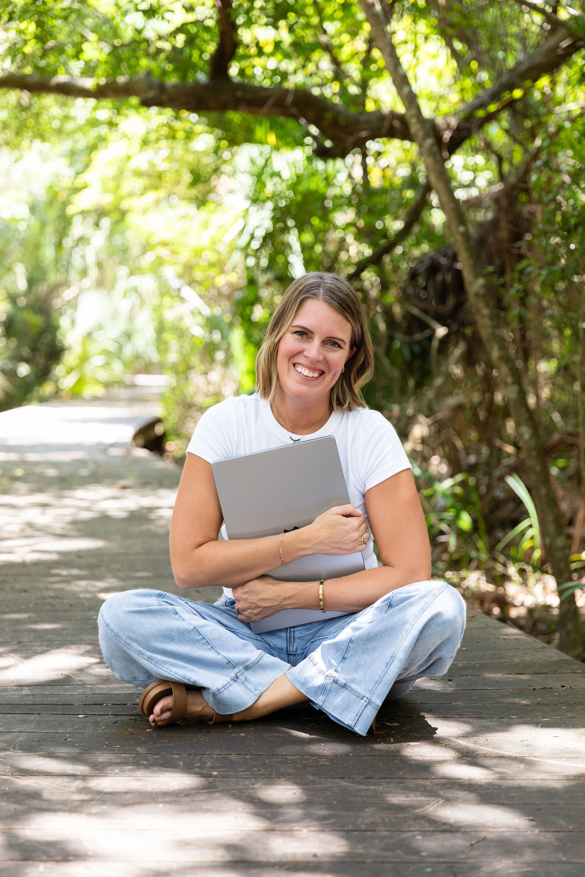 Callie, the founder of The Look & The Feel, sits cross legged on a shaded path holding her Macbook