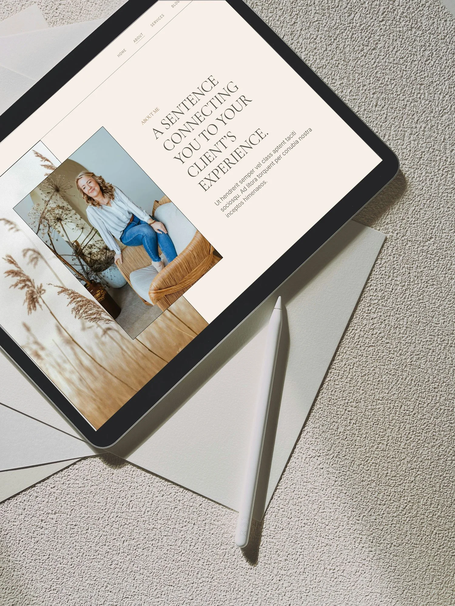 Digital tablet displaying a website with an image of a woman sitting on a wicker chair and text about connecting with clients, placed on a textured surface with a white stylus beside it.