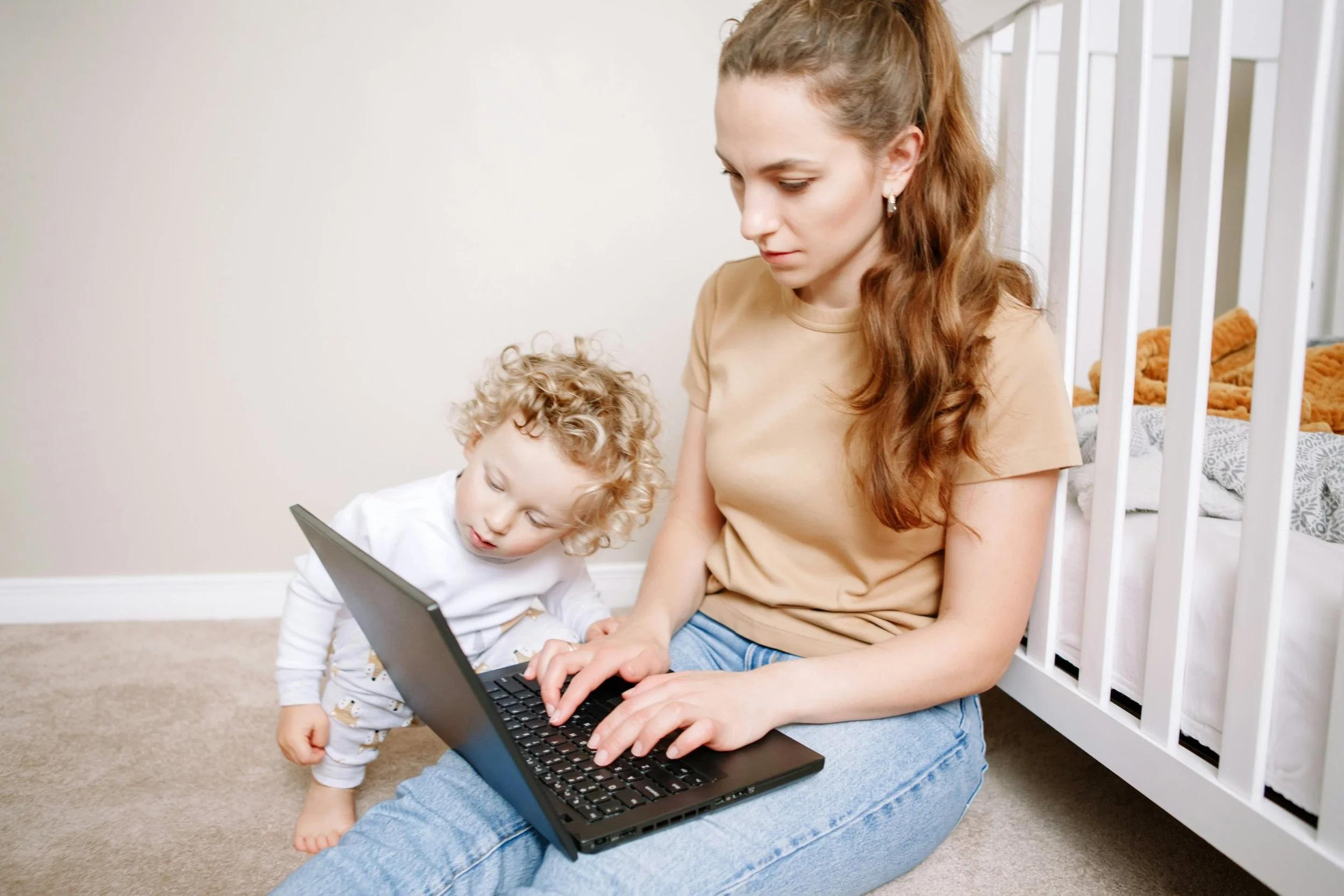 A mother working on a laptop in her child's nursery