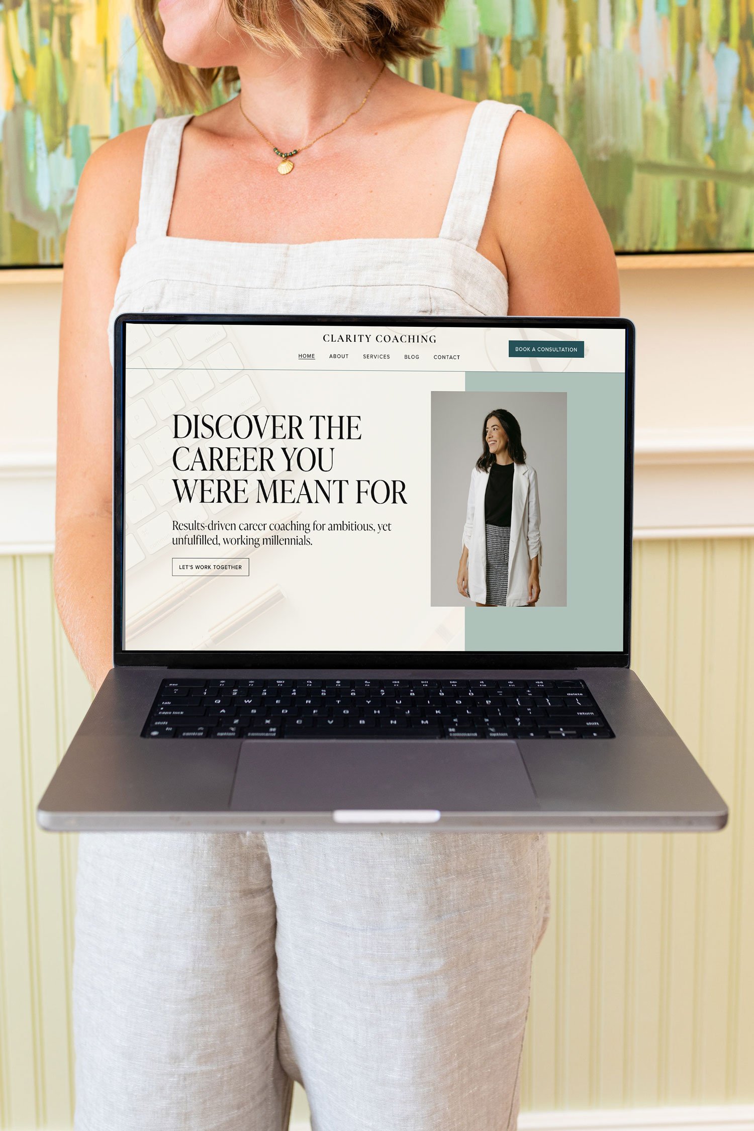 A woman in a white sleeveless top and beige pants holds a laptop displaying a website for career coaching, with the headline "Discover the career you were meant for" and an image of a smiling woman.