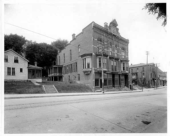 This is the Jassoy Building located on 3rd Street and Chestnut. It was built in 1886. It is a three-story frame red brick veneer with a Queen Anne Style. It has a flat roof and a stone banding between the floors along with bay windows on the second floor. This building still stands today at the base of the Chestnut Street Stairway. The streetcar tracks are visible in the foreground. The date of the photograph is 1918. Photo credit is Mr. John Runk, courtesy of The Stillwater Public Library, John Runk Collection.