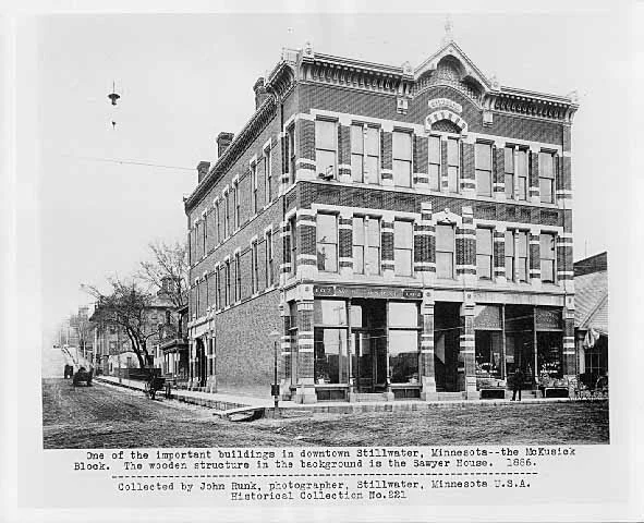The McKusick Block, located on the Northwest corner of Myrtle and Main Streets. This photo was taken in 1886 and is sourced from the John Runk Collection, courtesy of the Stillwater Public Library. In the background you are able to see the Sawyer House. The streets were dirt at that time. Narrative by Robert Molenda The McKusick Building was built in 1880. You have to exercise your history detective skills in order to see the ghost of the old building hidden in the building today. Presently, it is a two story building that has a marble facing. It covers the masonry brick frontage of the old building, but with a little effort, you can see the ghost of the old building that originally stood at this location. To Read More About The McKusick Building, Click or Tap on the Highlighted Text.
