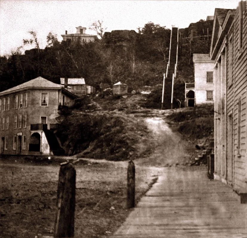 This is a very early (1866) view up the south hill stairs. The stairs were wooden at this time and it was before the construction of the brewery of Joseph Wolf. The home at the top of the hill still stands today. The three story building at the street level is gone.