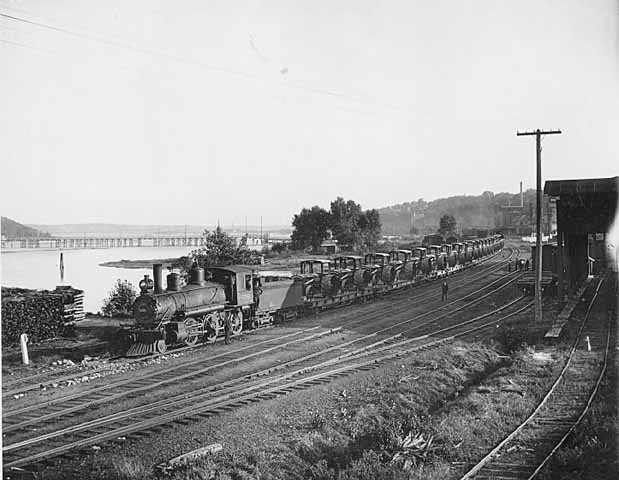 This is a John Runk photo taken behind the Northwest Thresher Manufacturing Company Building ca.1910. The view is toward the south with the wooden pontoon bridge in the background. Access to the railway was important to Stillwater during and after the lumber era.