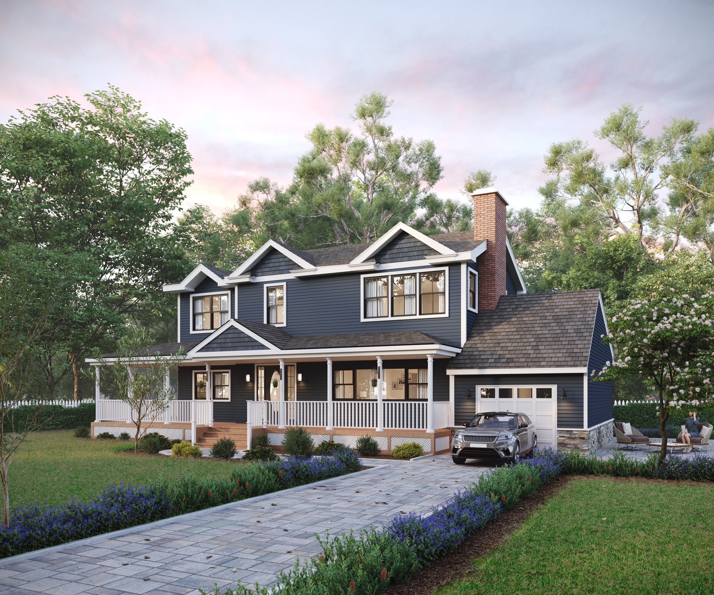A large, modern blue two-story house with white trim and a porch, surrounded by a landscaped yard with flowers, trees, and a stone driveway leading to an attached garage, with a man sitting outdoors on a patio chair.
