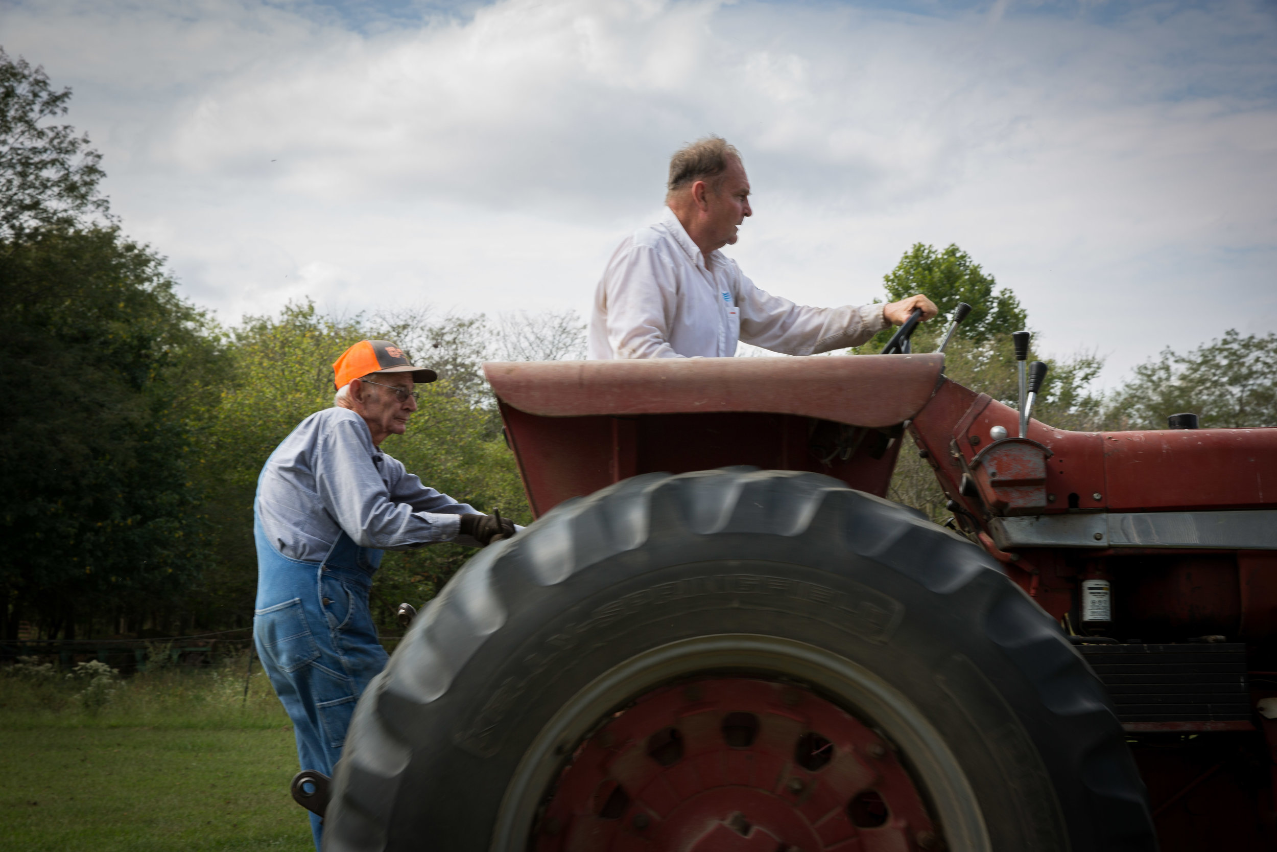 Carl hitches a ride as Mike drives the tractor to the grain silo they are cleaning out for the corn harvest.