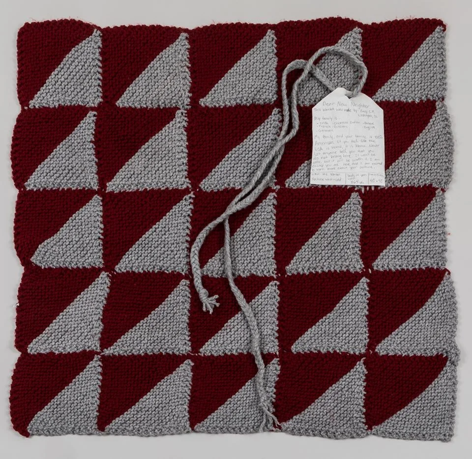 (IMAGE DESCRIPTION: Welcome Blanket no. 00008 is a 5X5 gray and red repeated half square triangle pattern comes from Atlanta, GA with a note of welcome: "My family, and your family, is 100% American. If you feel like the USA is home, it is home. Never let anyone tell you that you do not belong here. It won't be easy, but it will be worth it. I am excited you are here, and I am excited to learn more about your culture.” )
