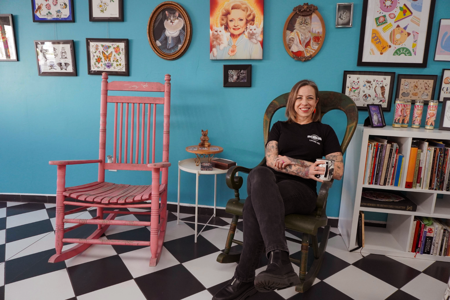 Image of Stephanie Robinson sitting in a rocking chair in front of art at Roses and Rivets Tattoo Shop in Santa Paula CA