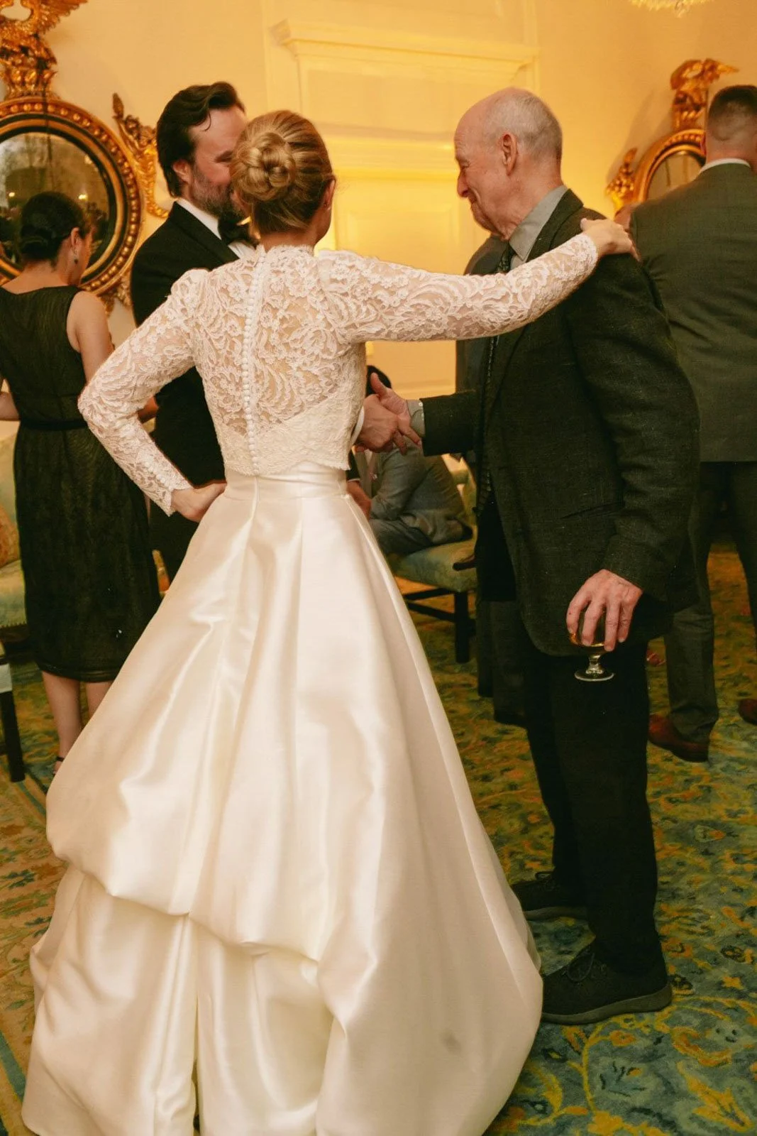 People greeting each other at a formal event, with a woman in a white wedding gown and a man in a suit.
