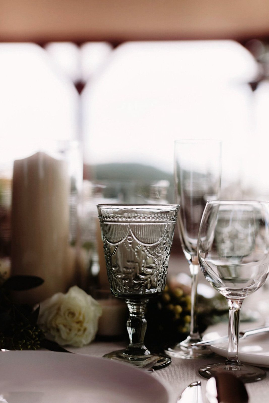 Decorative glassware and a white rose on a dining table, with candles and blurred background at Court Hill in The Berkshires.
