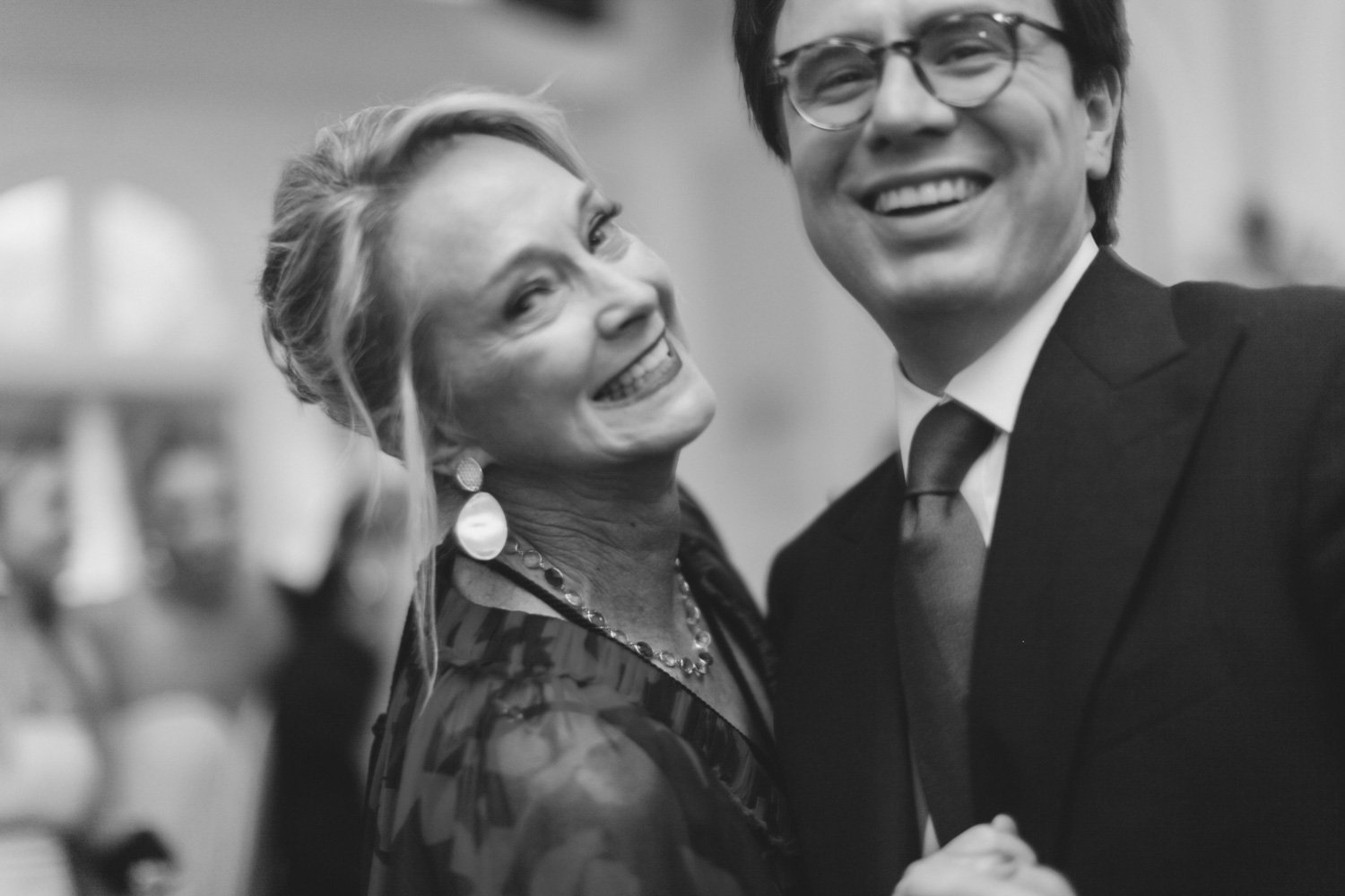 Black and white photo of a smiling older woman and a young man in a suit, holding hands.