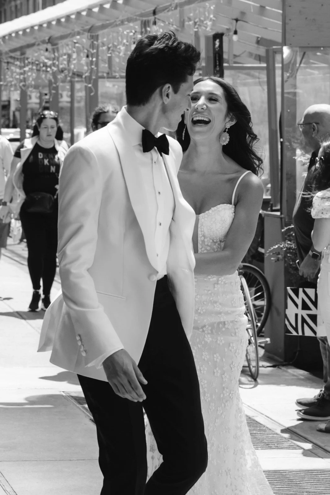 A joyful couple in wedding attire dancing outdoors, surrounded by onlookers and festive decorations.