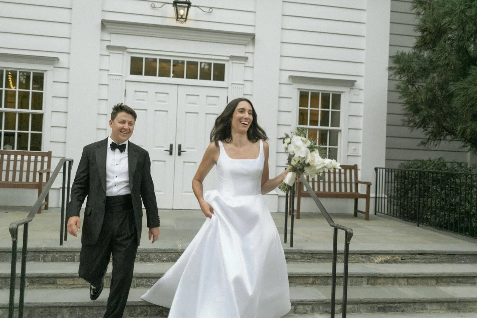 A bride in a white wedding gown holding a bouquet and a groom in a black tuxedo walking out of Stanwich Church in Greenwich, CT. 