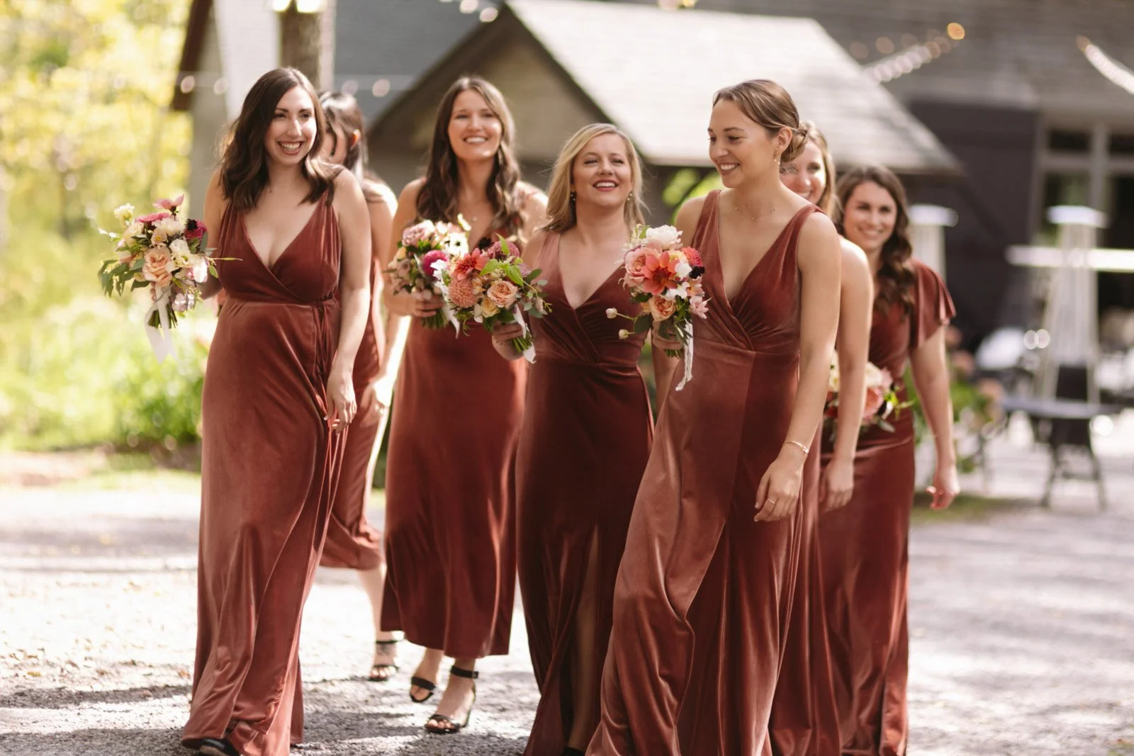 A group of women in maroon dresses walking outdoors, holding bouquets of flowers, smiling and enjoying a special occasion.
