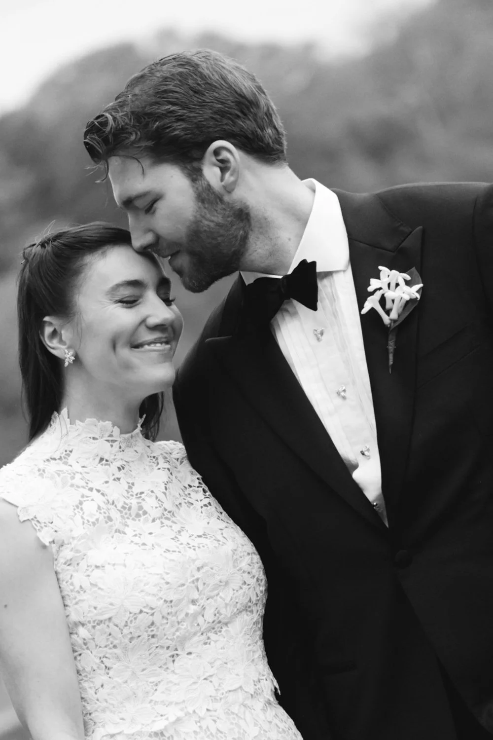 Black and white photo of a bride and groom on their wedding day, smiling and touching foreheads affectionately outdoor.