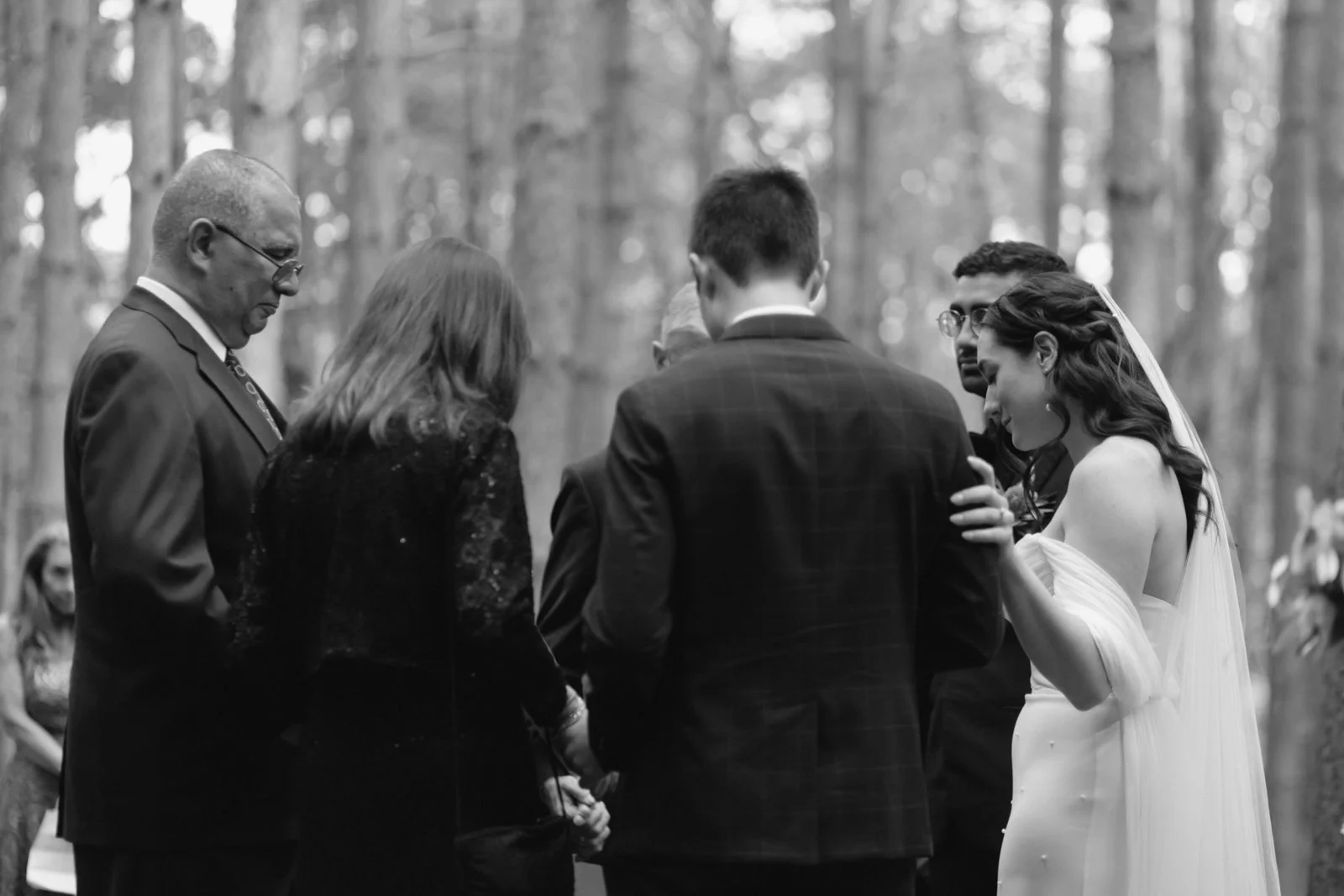 Black and white photo of a wedding ceremony with a bride, groom, and officiant in a wooded outdoor setting.