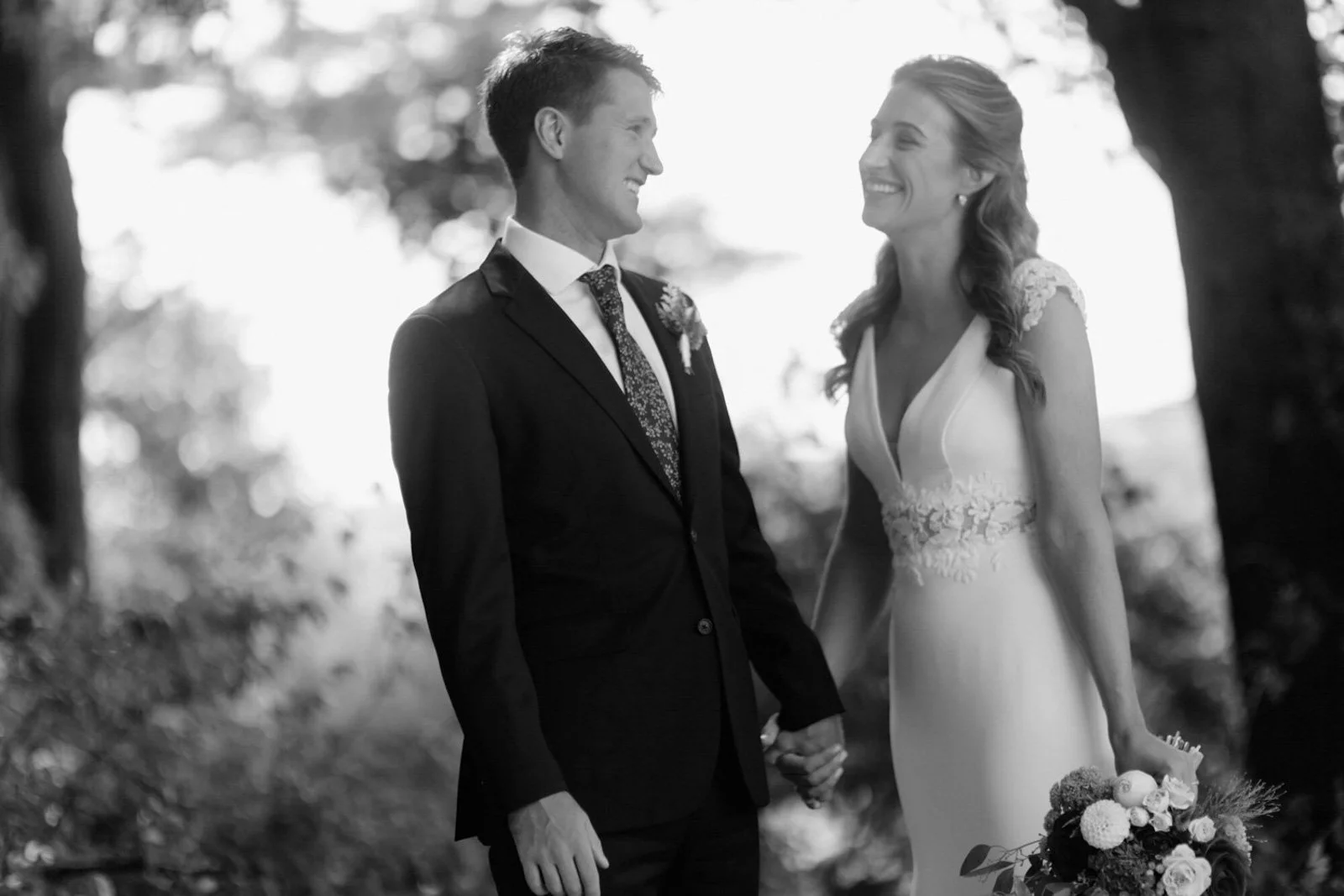 A black and white photo of a couple in wedding attire holding hands and smiling at each other outdoors at Court Hill in The Berkshires.