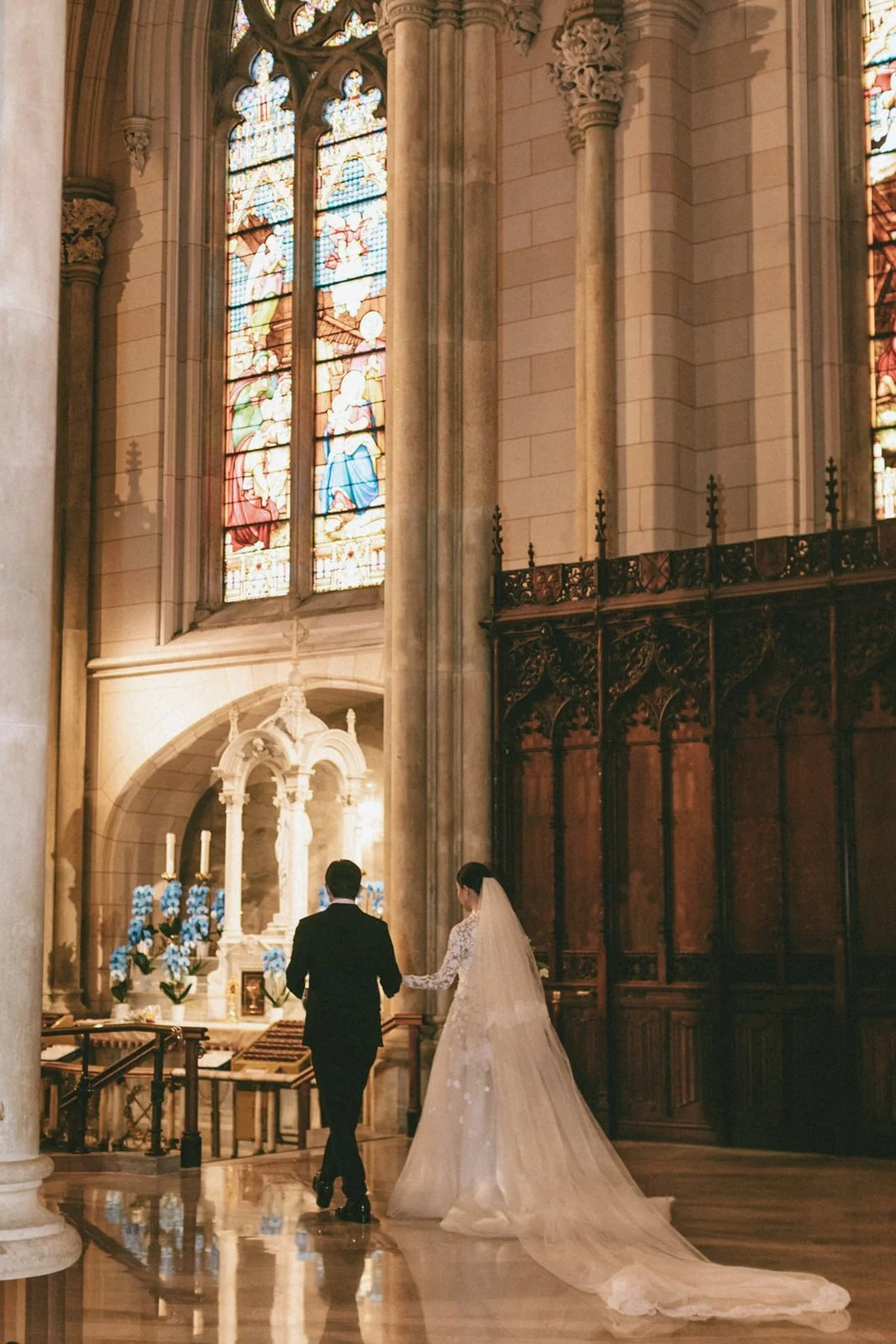A bride and groom holding hands inside a church with stained glass windows and wooden accents.