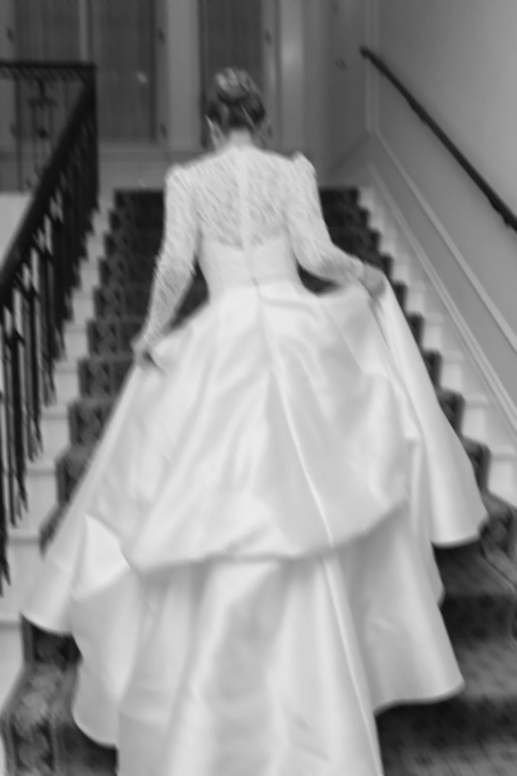 A woman in a white wedding dress walking up a staircase with a black railing.