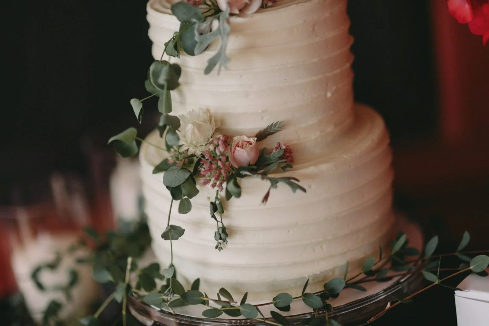 Close-up of a white wedding cake decorated with green leaves and pink and white flowers.