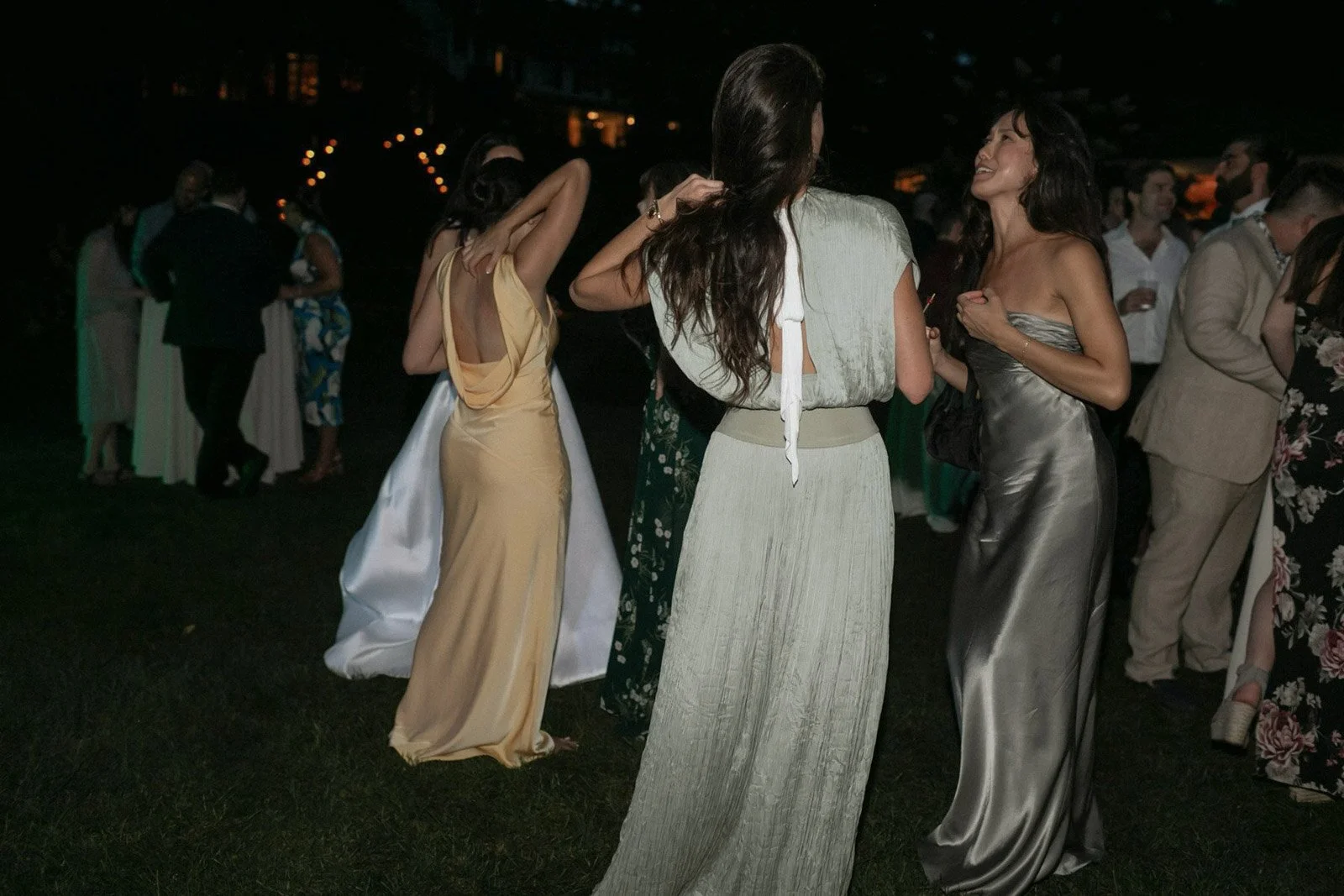 People at an outdoor evening event, dressed in formal and cocktail attire, engaging in conversation and socializing.