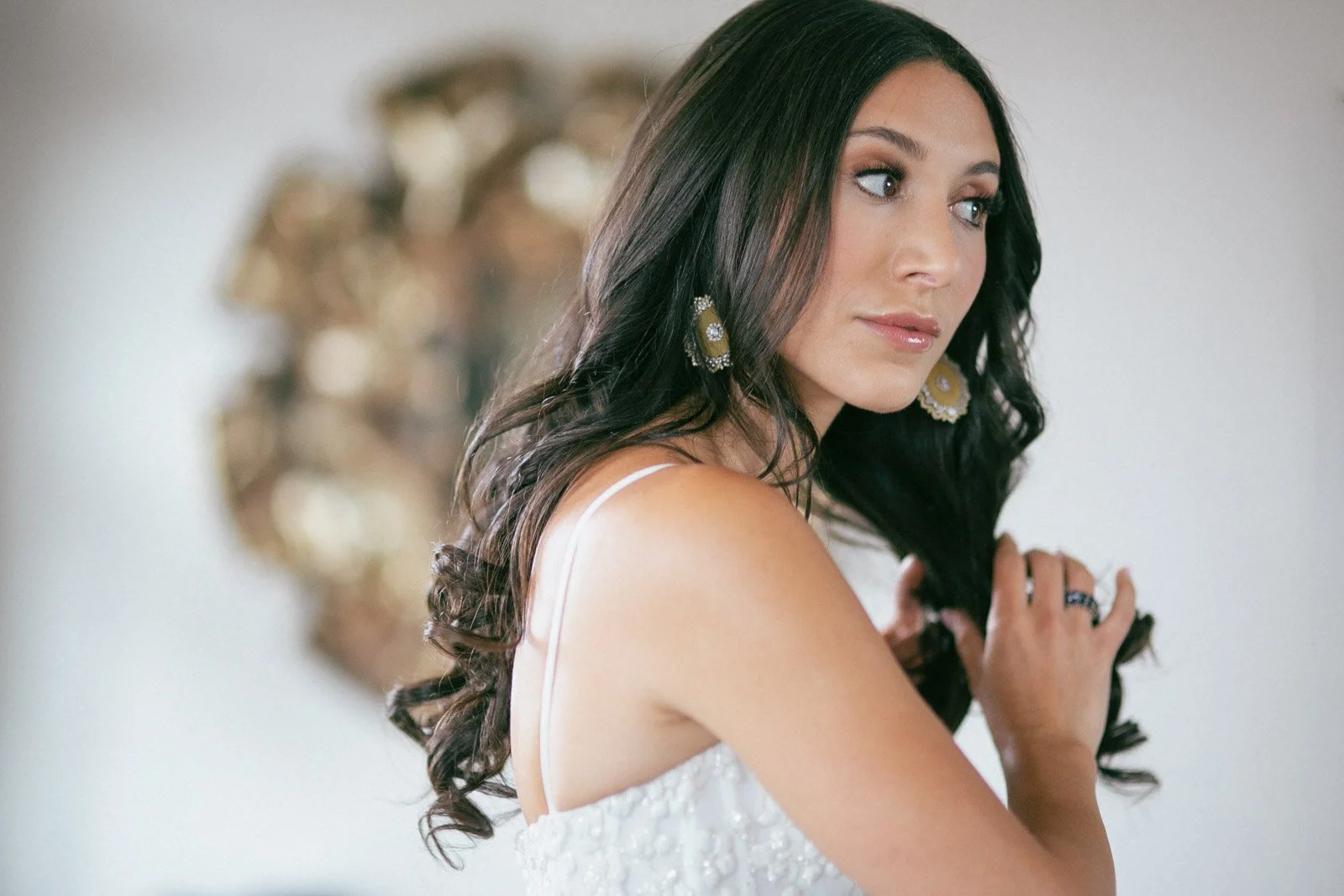 A young woman with long dark hair wearing earrings and a white dress with beadwork, looking to her right.
