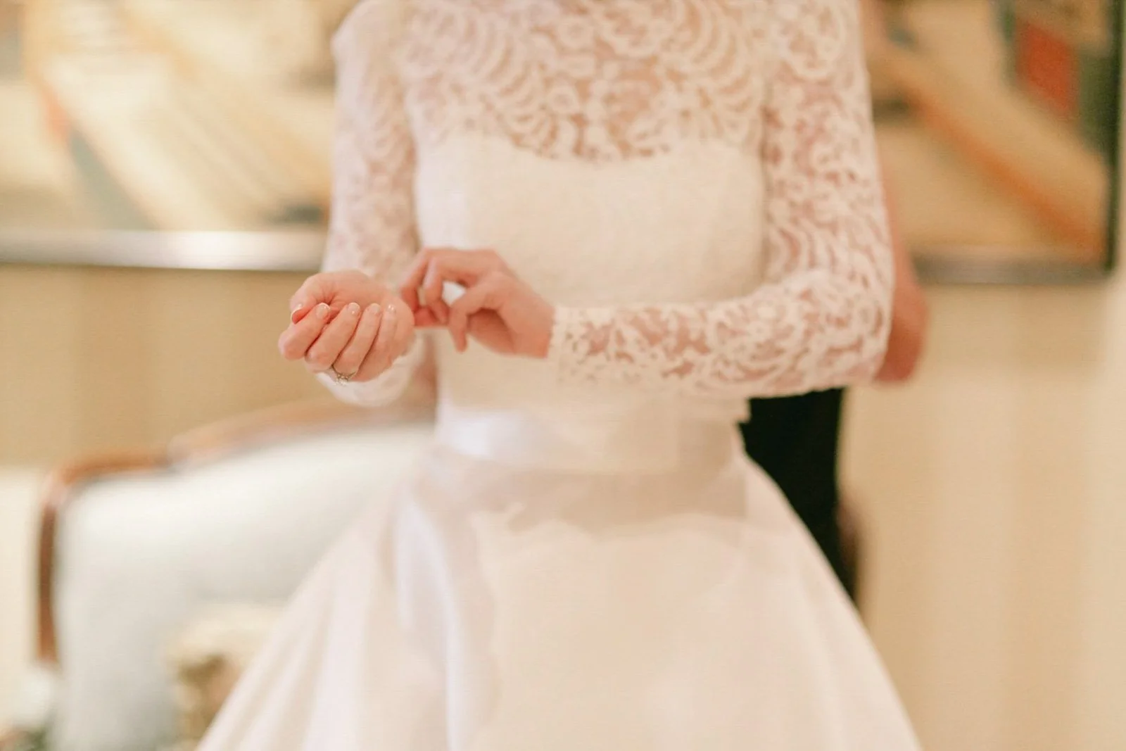 Woman wearing a white lace wedding dress adjusting her sleeve inside a building.