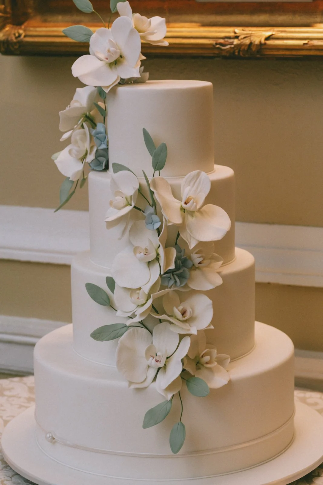 A three-tier white wedding cake decorated with cascading white orchids and green leaves.