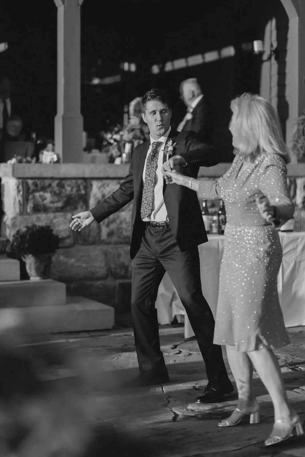 A man in a suit dancing with a woman in a dress at a wedding reception.
