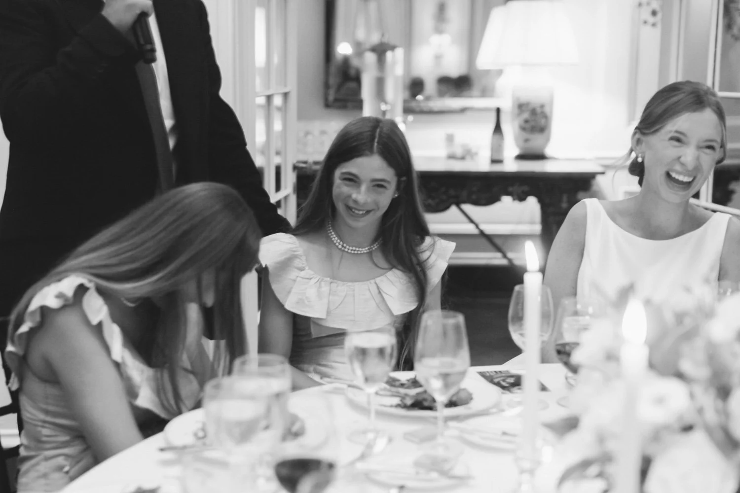 People at a dinner table, smiling and laughing, with candles and glasses of water or wine.