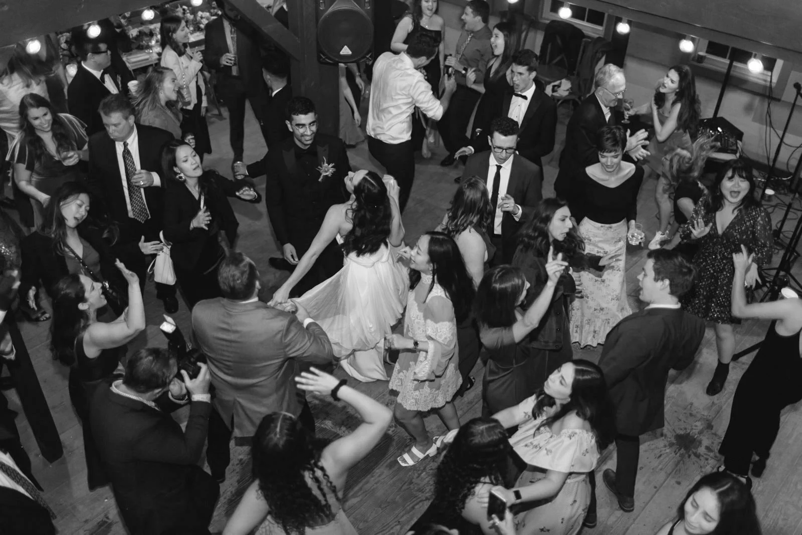 People dancing and socializing at a party or celebration with a DJ or music setup in the background.