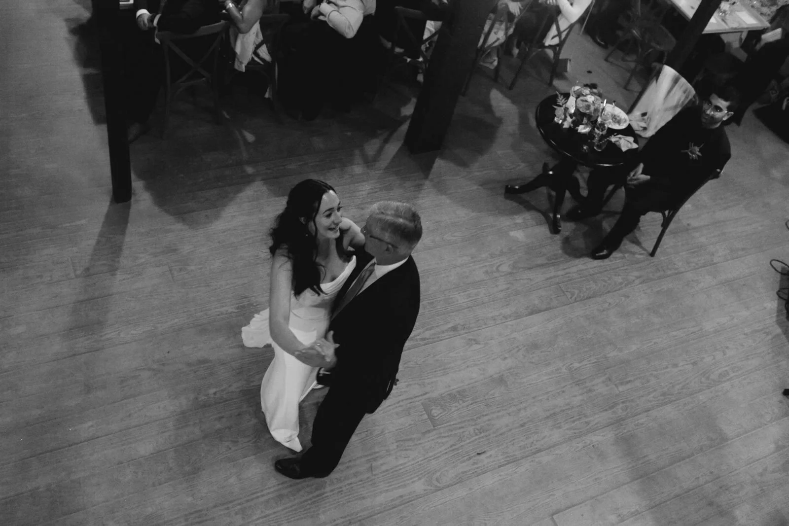 A bride and groom dancing at their wedding reception, seen from above in black and white.