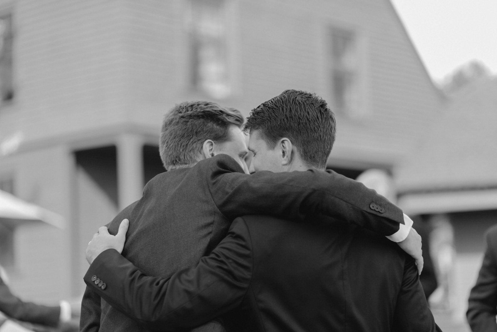 Two men in suits hugging each other closely outside a house.